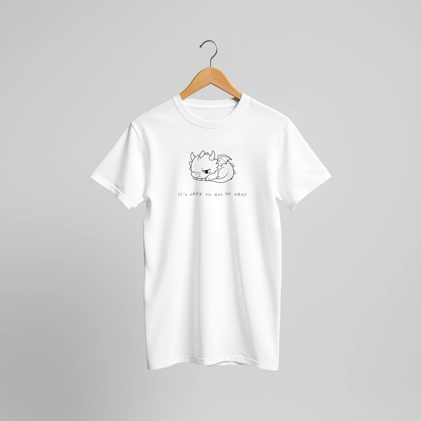 White dragon mental health t-shirt on wooden hanger against neutral background