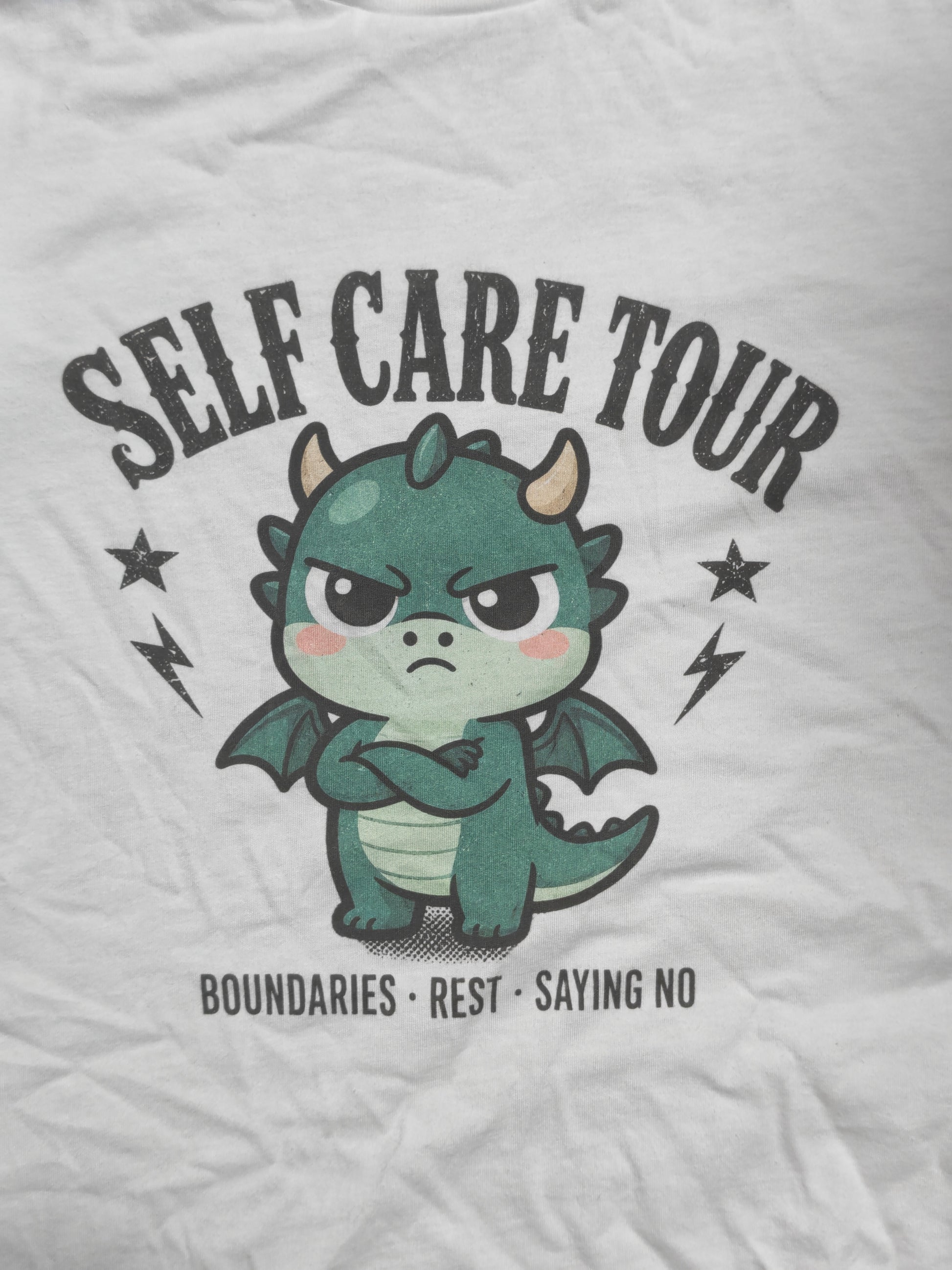 Macro close-up of the Self Care Tour print on real white cotton, showing the distressed lettering, halftone shading and visible fabric weave.